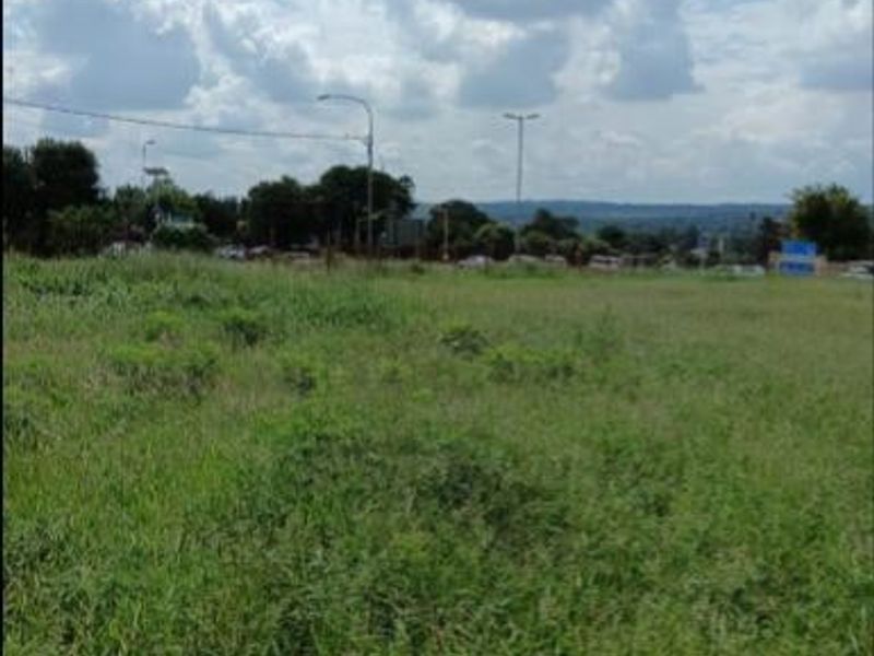 A view of a vacant residential plot featuring open grassland with surrounding street infrastructure and distant landscape views.