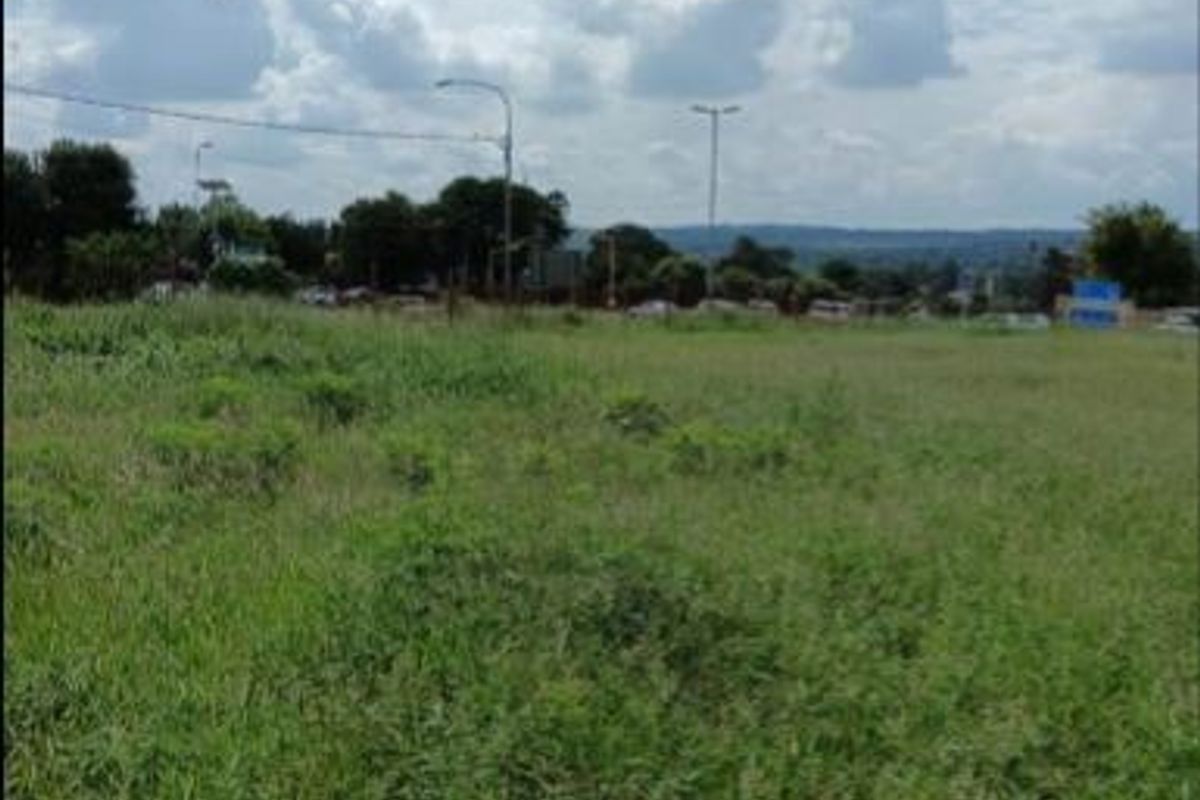 A view of a vacant residential plot featuring open grassland with surrounding street infrastructure and distant landscape views.