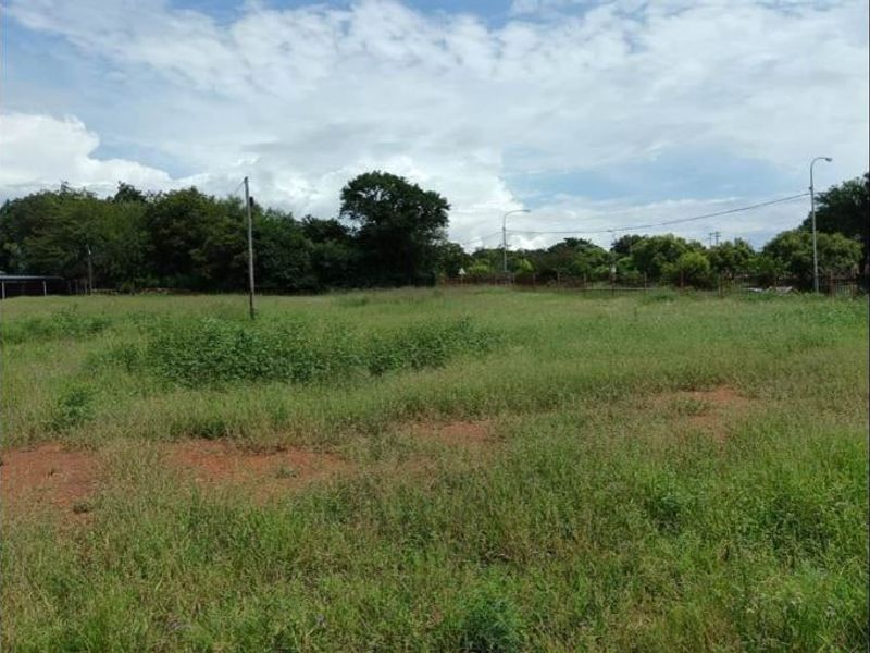 A vacant residential plot of land featuring natural grass cover, perimeter fencing, and utility poles, offering a clear space for future development.
