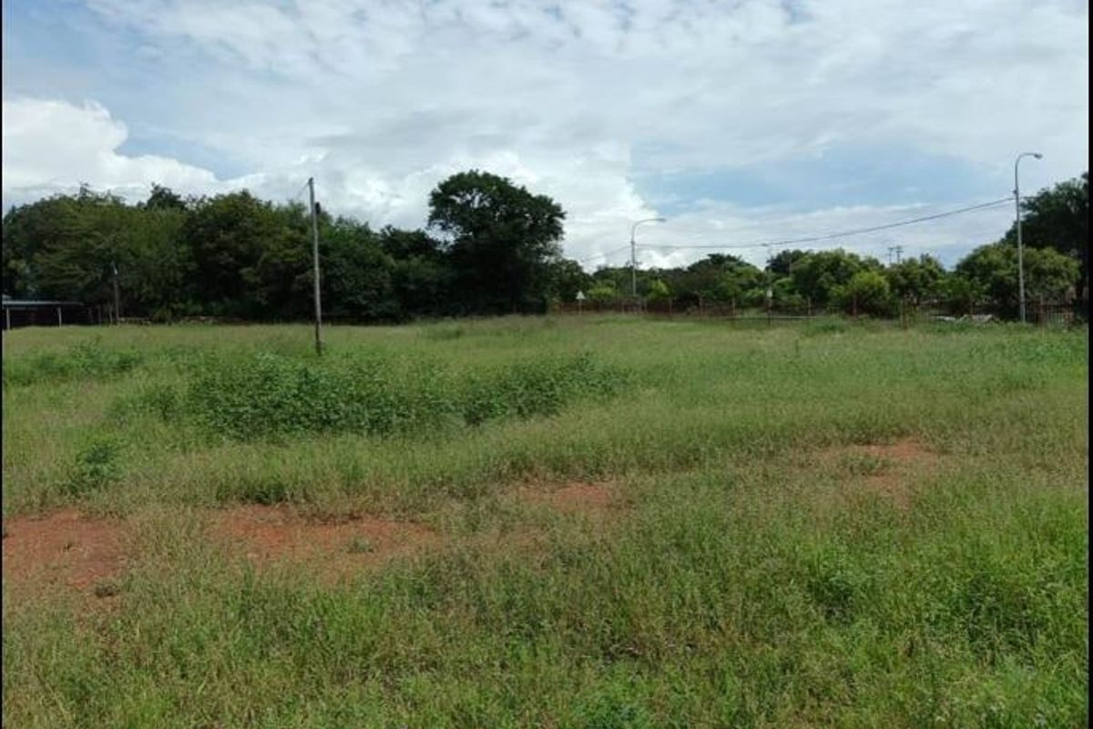 A vacant residential plot of land featuring natural grass cover, perimeter fencing, and utility poles, offering a clear space for future development.