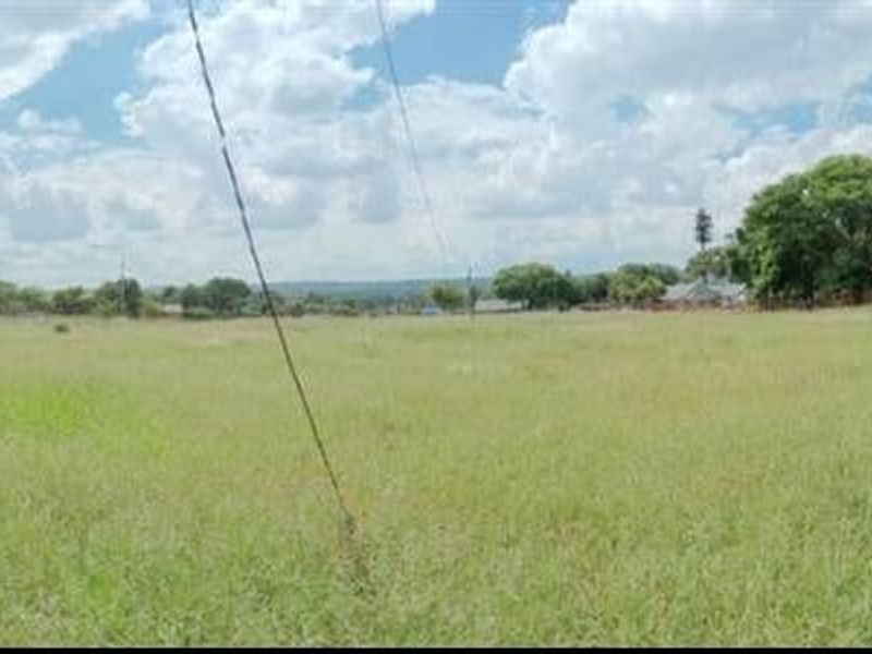 A wide panoramic view of a vacant residential plot featuring natural grass coverage and perimeter boundary fencing.