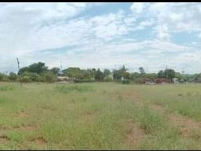 A wide panoramic view of a vacant residential plot featuring natural grass coverage and perimeter metal fencing.