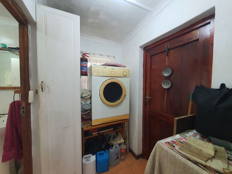A functional laundry area featuring tiled flooring, a built-in cupboard, and a timber door, showing signs of ceiling wear and maintenance requirements.