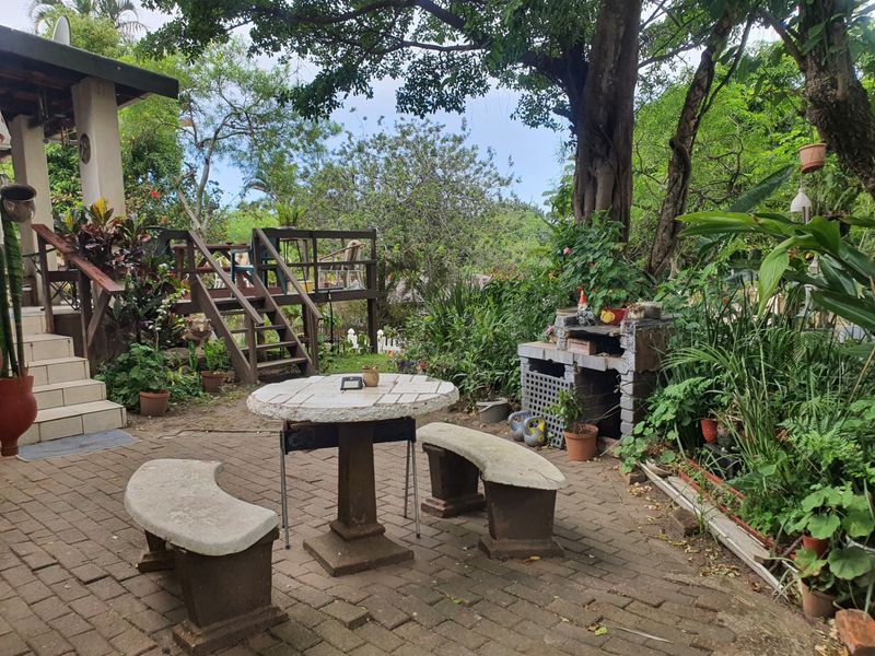 Outdoor patio area featuring brick paving, a raised timber deck, and a built-in masonry barbecue set within a lush garden environment.