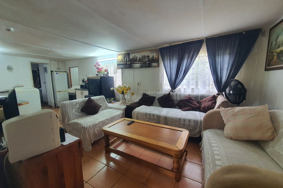 A living room area featuring tiled flooring and natural light through window treatments, offering a functional space with potential for cosmetic updates.