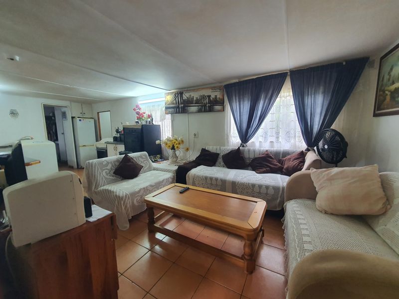 A living room area featuring tiled flooring and natural light through window treatments, offering a functional space with potential for cosmetic updates.