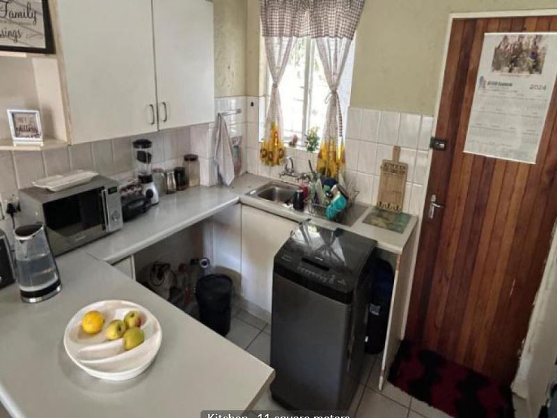 Compact kitchen featuring built-in cabinetry, laminate countertops, and a stainless steel sink, offering a functional layout with direct access to an exterior door.