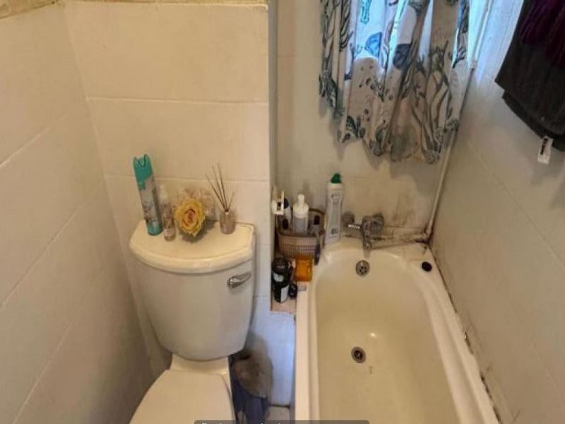 A compact bathroom featuring a standard toilet and bathtub with tiled walls, currently showing signs of wear and requiring maintenance or renovation.