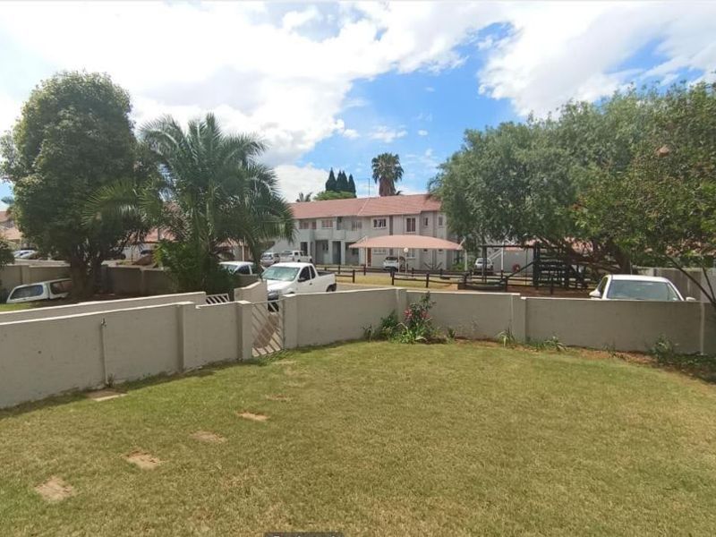 A view of a private rear garden area featuring a well-maintained lawn and a solid boundary wall with a pedestrian gate.
