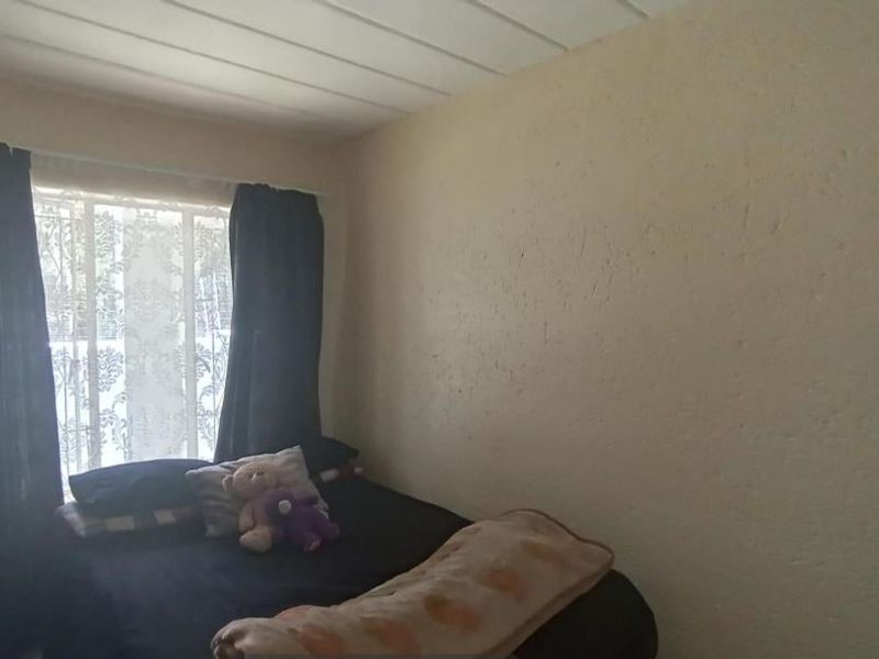 A bedroom featuring textured walls, a panelled ceiling, and a window fitted with a security gate.