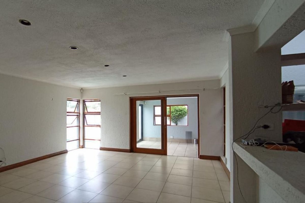 Spacious, empty living area featuring neutral tiled flooring, textured walls, and sliding glass doors leading to an adjacent sunroom or patio space.