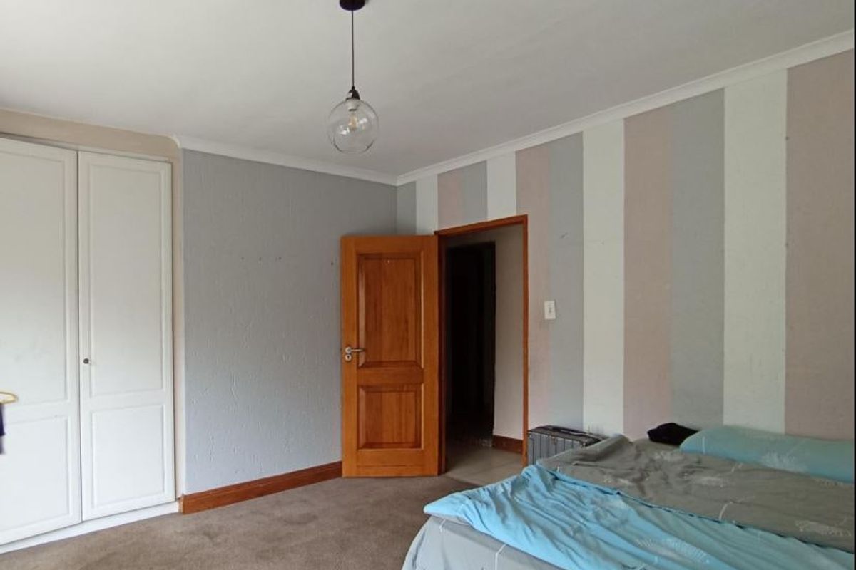 A bedroom featuring built-in wardrobes, carpeted flooring, and a pendant light fixture, offering a functional space ready for cosmetic updates.