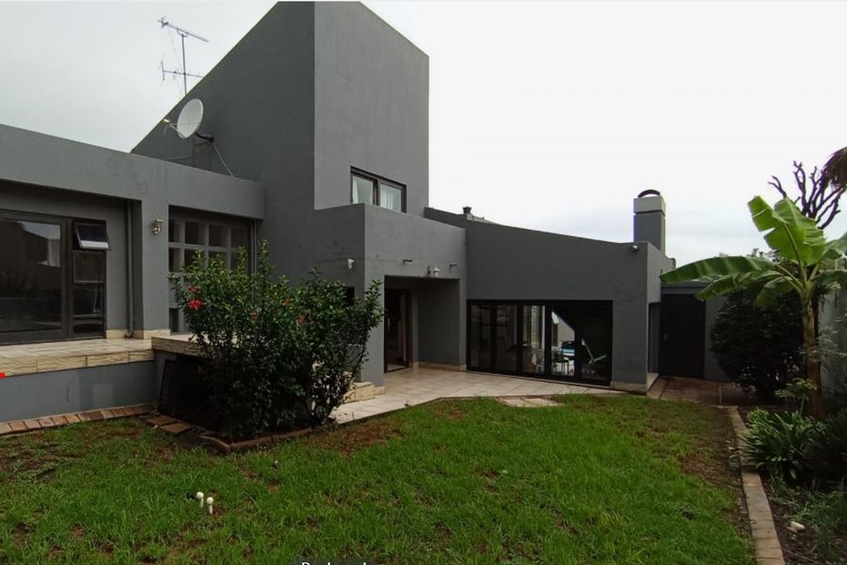 Rear view of a modern grey-painted house featuring a tiled patio area, sliding glass doors, and a private garden space.