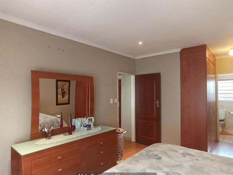 Spacious bedroom featuring built-in cupboards, laminate flooring, and direct access to an en-suite bathroom.