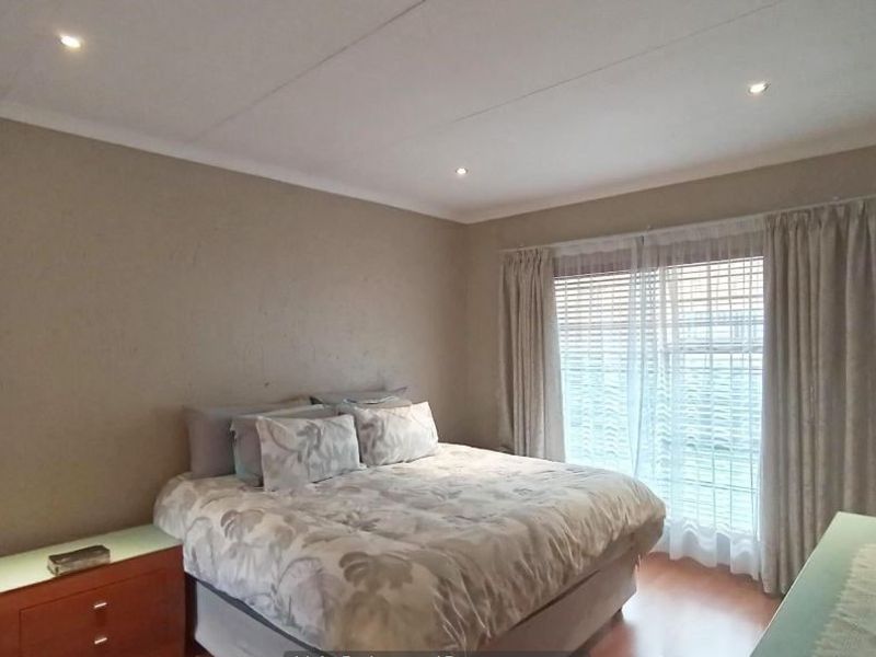 A bedroom featuring laminate flooring, recessed downlighting, and large windows with curtain tracks, providing a functional and neutral living space.