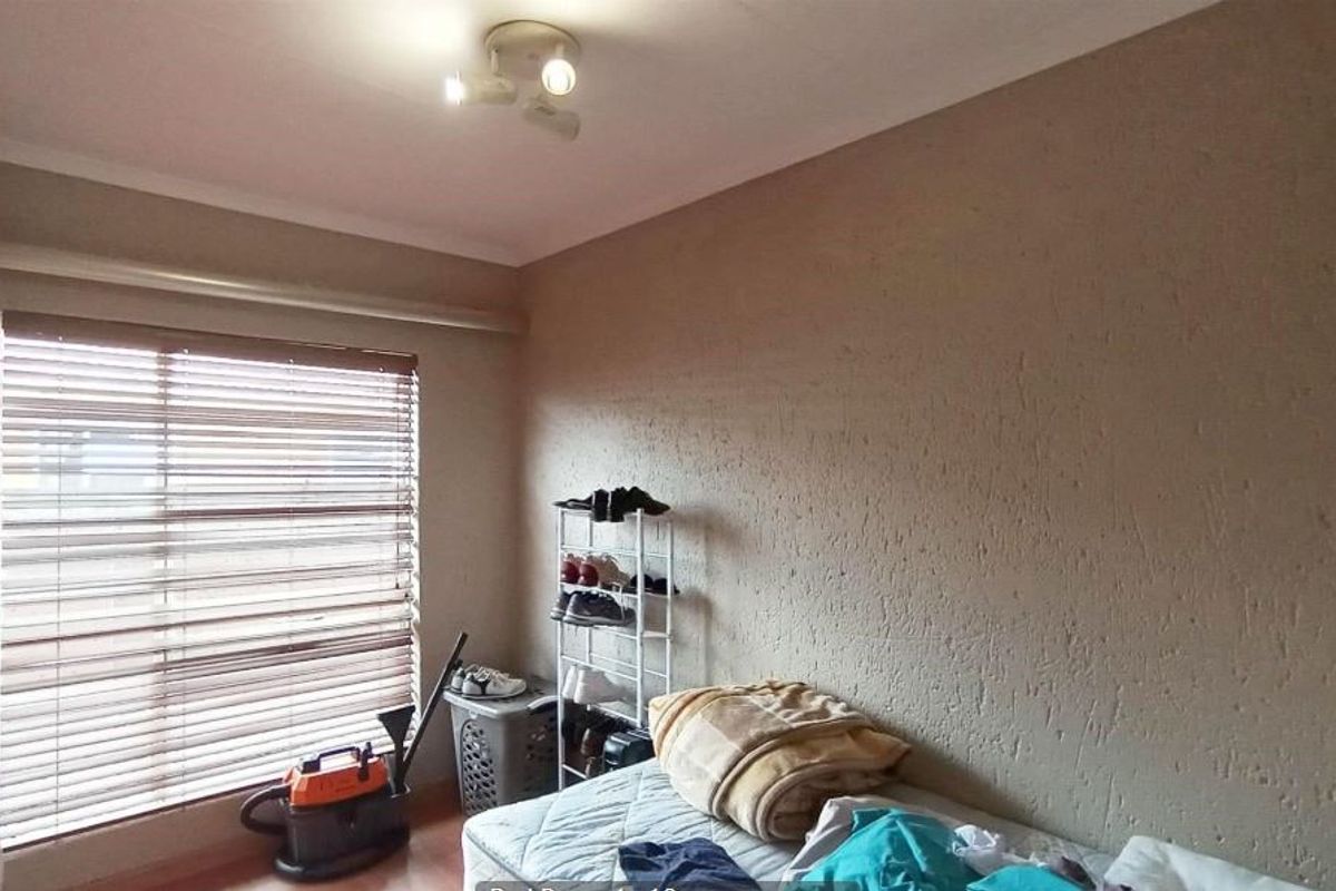 A standard bedroom featuring laminate flooring, a ceiling-mounted spotlight fixture, and venetian blinds on the window.