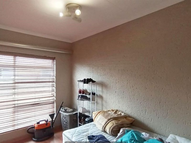 A standard bedroom featuring laminate flooring, a ceiling-mounted spotlight fixture, and venetian blinds on the window.