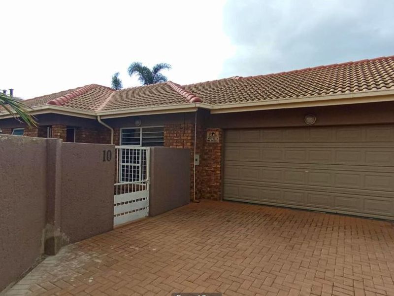 Front elevation of a brick-faced house featuring a paved driveway, double garage, and secure gated entrance.