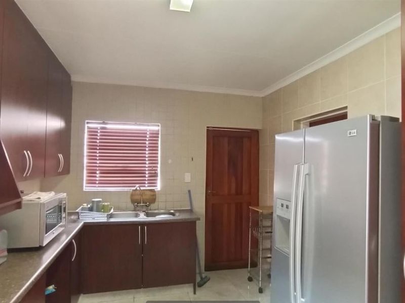 A functional kitchen featuring dark wood cabinetry, tiled backsplash, double sink, and tiled flooring, providing a practical workspace for daily meal preparation.