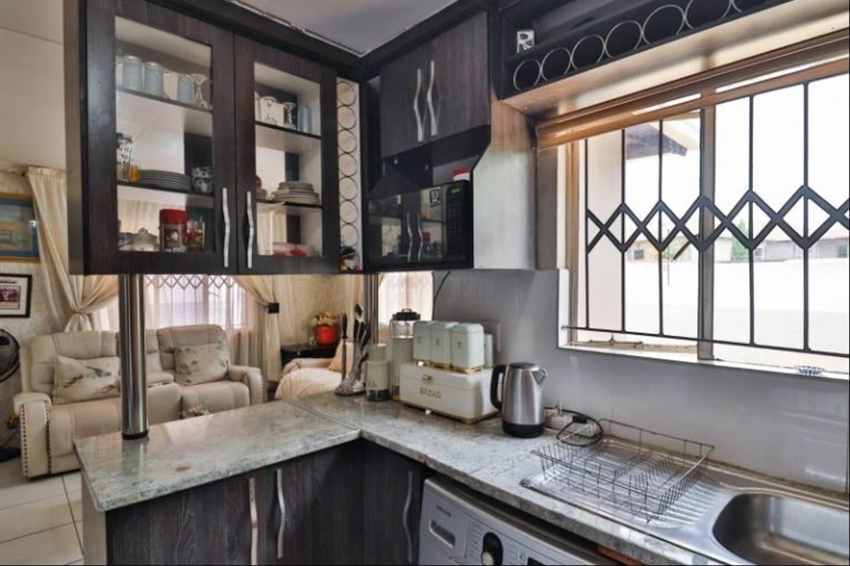 A functional kitchen featuring dark wood cabinetry, granite countertops, and a stainless steel sink, with integrated microwave and security bars on the window.