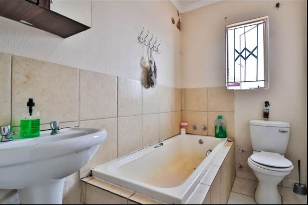 A dated bathroom featuring a pedestal basin, built-in bathtub, and toilet, requiring cosmetic updates and repairs to wall finishes and fixtures.