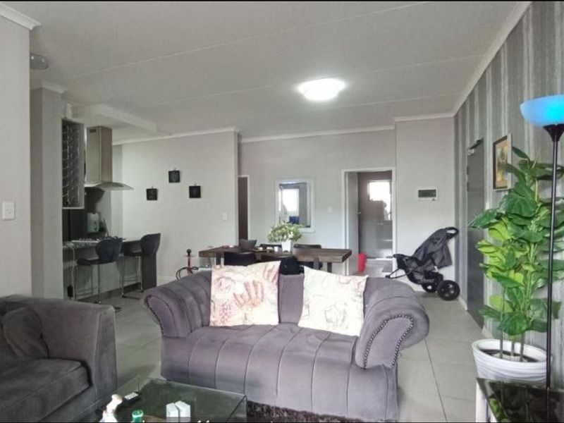 Open-plan living and dining area featuring tiled flooring, coved ceilings, and a functional kitchen space with built-in cabinetry and extractor fan.