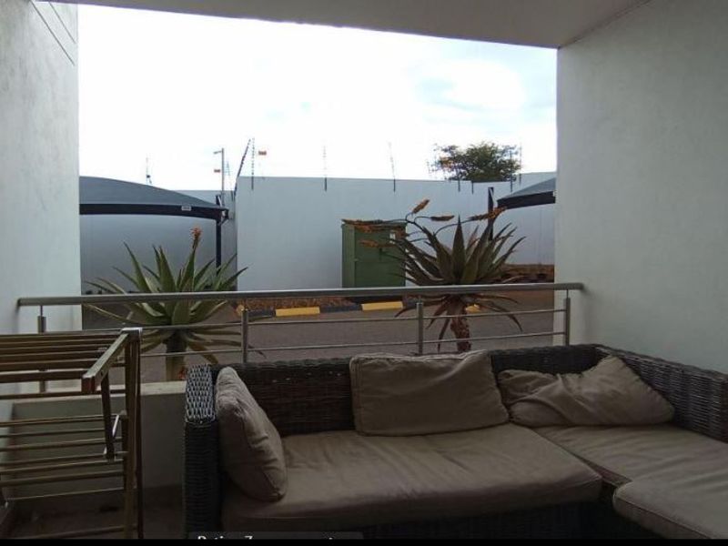 A covered balcony area featuring a stainless steel balustrade, providing an outdoor space overlooking the complex parking area.