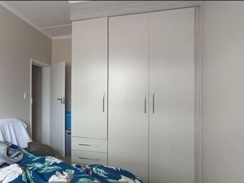 A bedroom featuring a modern, neutral-toned built-in wardrobe with integrated drawers and sleek metal handles.