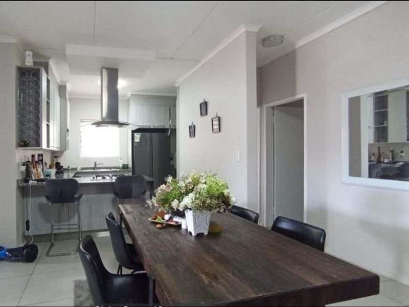 Open plan living and dining area featuring a modern kitchen with island, stainless steel extractor fan, and neutral tiled flooring throughout.