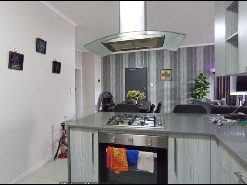 Open plan kitchen featuring a central island with built-in oven, gas hob, and modern extractor fan, seamlessly flowing into the living and dining area.
