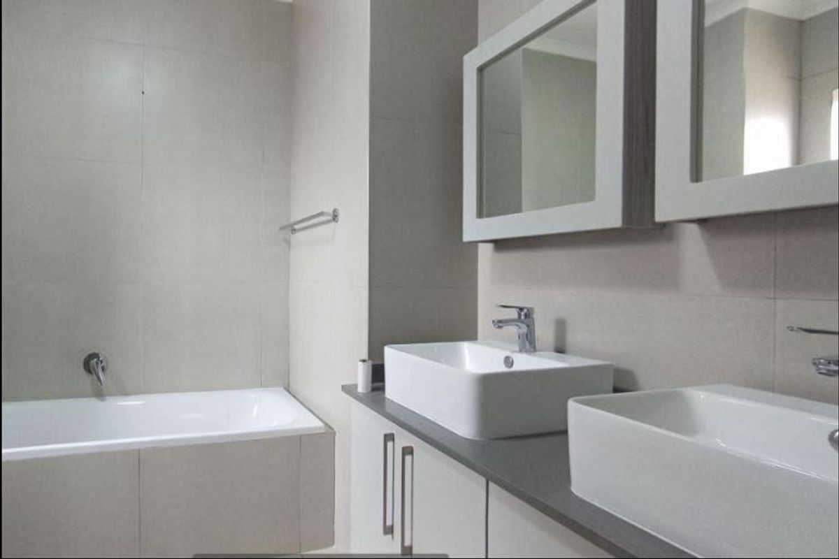 Modern bathroom featuring a double vanity with vessel sinks, wall-mounted faucets, and a built-in bathtub with neutral wall tiling.