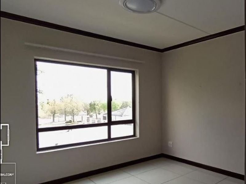 A bright, empty bedroom featuring neutral tiled flooring, dark skirting boards, and a large window providing natural light.