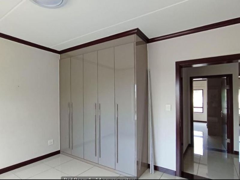 A clean, empty bedroom featuring modern high-gloss built-in cupboards, tiled flooring, and dark wood-finish door frames and skirting.