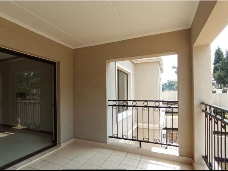 A covered balcony featuring tiled flooring and a wrought iron balustrade, accessible via a large sliding glass door.