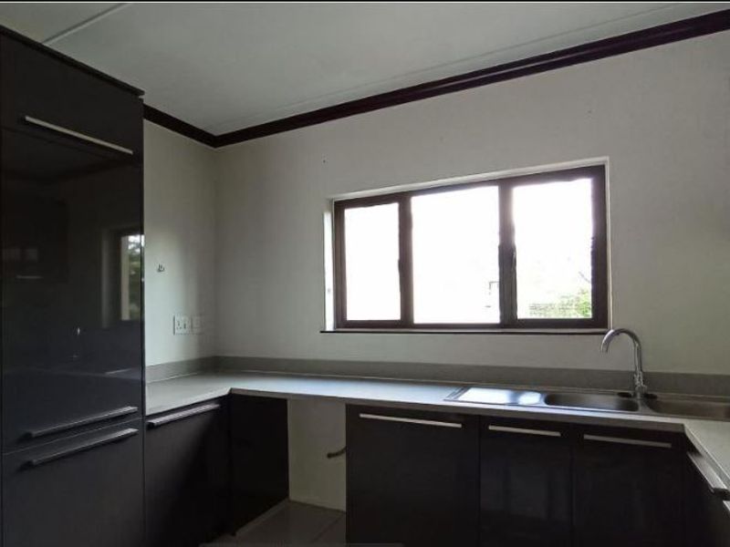A clean, modern kitchen featuring dark high-gloss cabinetry, ample countertop space, a stainless steel sink, and large windows providing natural light.