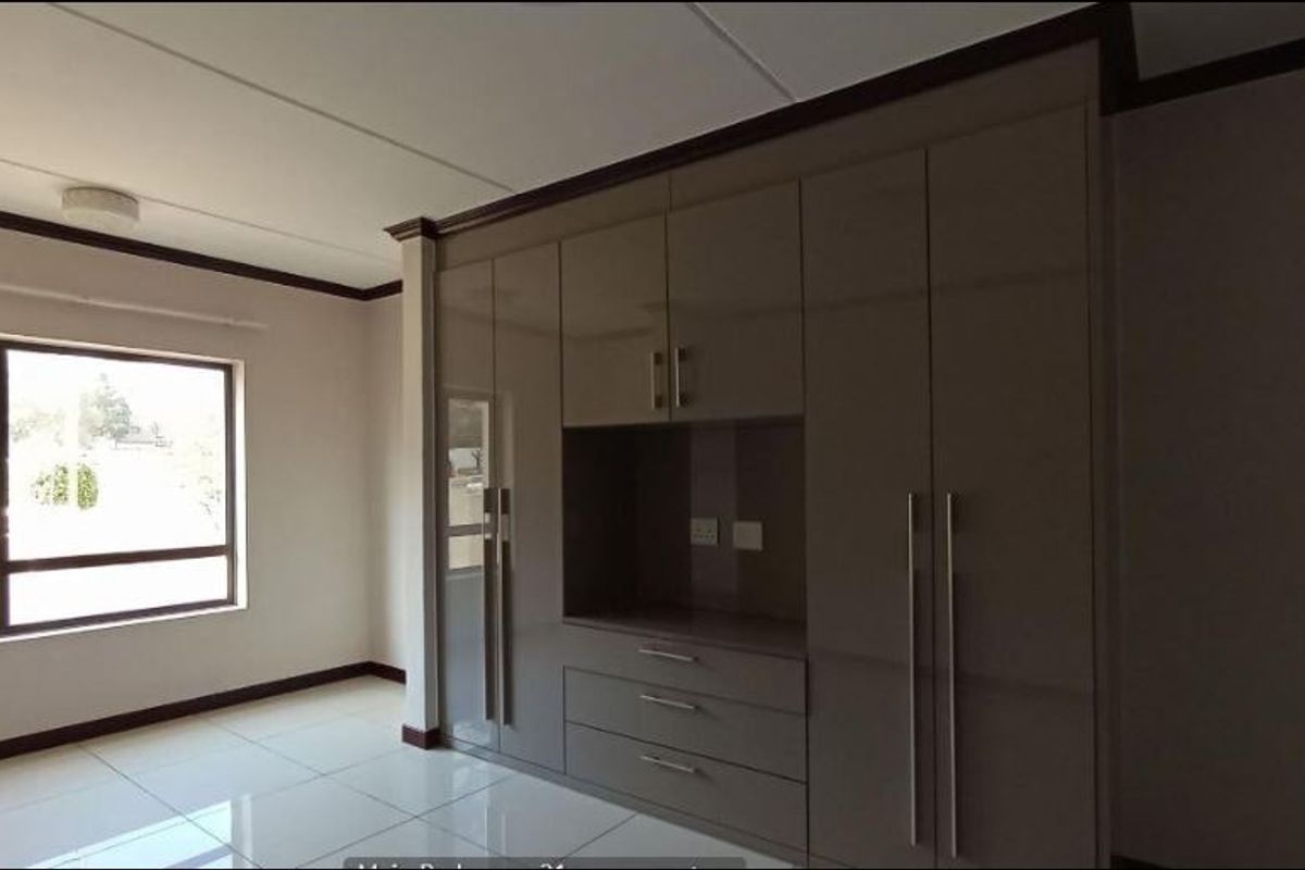 Spacious bedroom featuring modern high-gloss built-in cupboards, neutral tiled flooring, and large windows providing ample natural light.