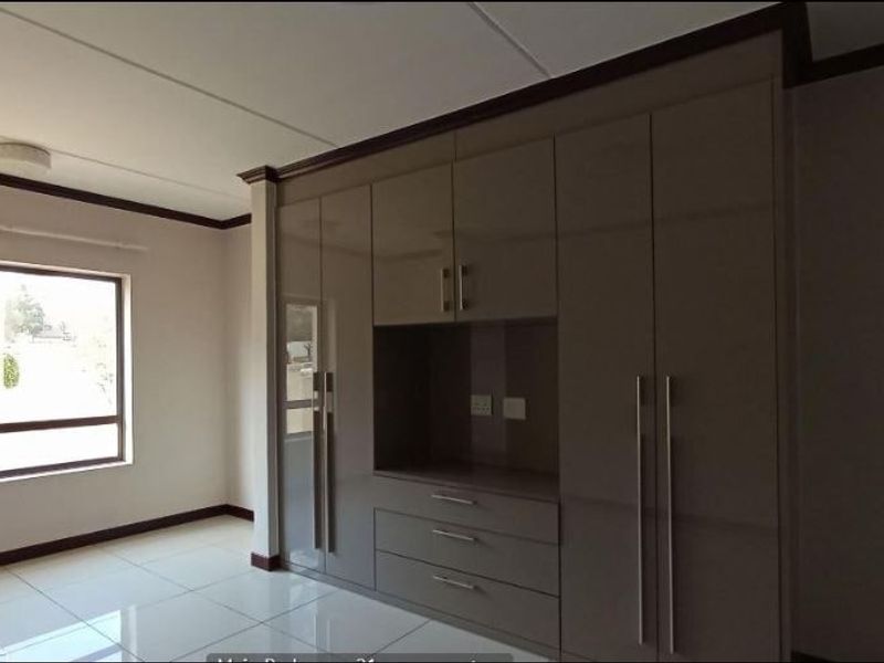 Spacious bedroom featuring modern high-gloss built-in cupboards, neutral tiled flooring, and large windows providing ample natural light.