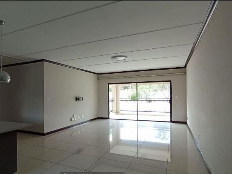 Spacious open-plan living area featuring neutral tiled flooring, modern pendant lighting, and large sliding glass doors leading to an outdoor balcony.