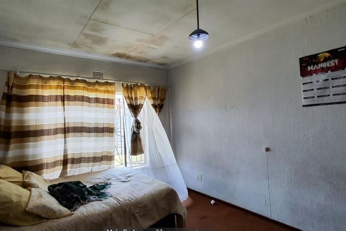 A bedroom featuring a security gate on the window, requiring ceiling and wall repairs due to visible water damage and surface deterioration.