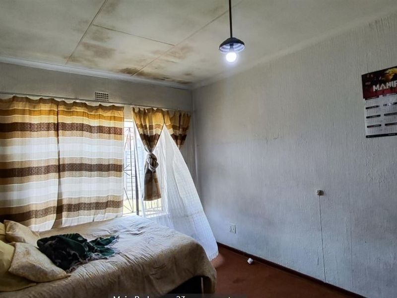 A bedroom featuring a security gate on the window, requiring ceiling and wall repairs due to visible water damage and surface deterioration.