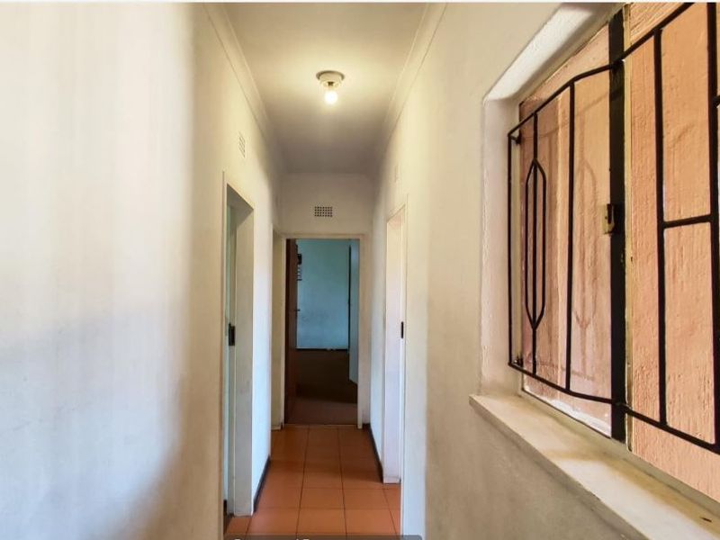 A functional hallway featuring tiled flooring, coving, and a security gate on the window, providing access to multiple rooms.
