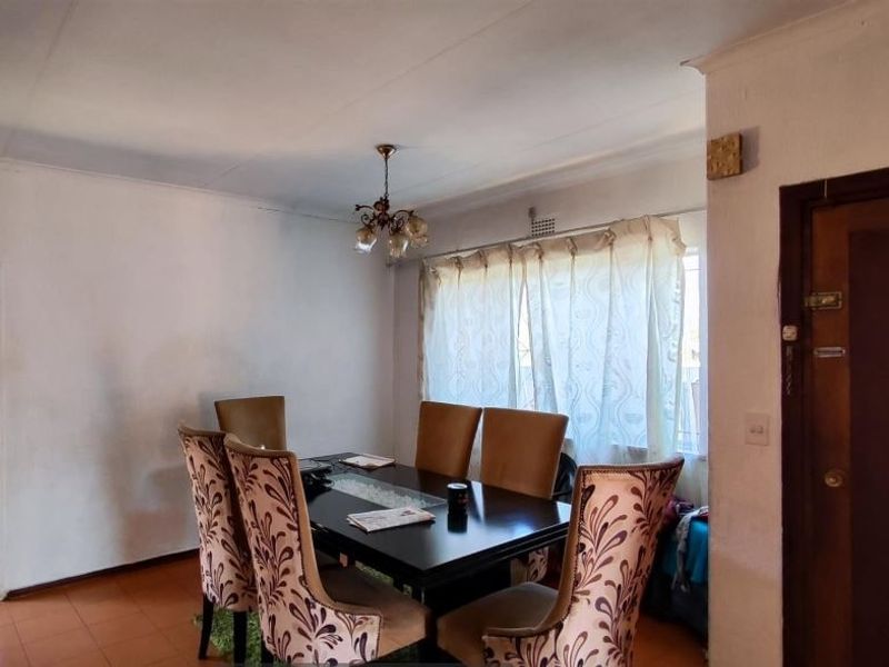 A dining room featuring tiled flooring, a ceiling light fixture, and access to an adjacent room through a timber door.