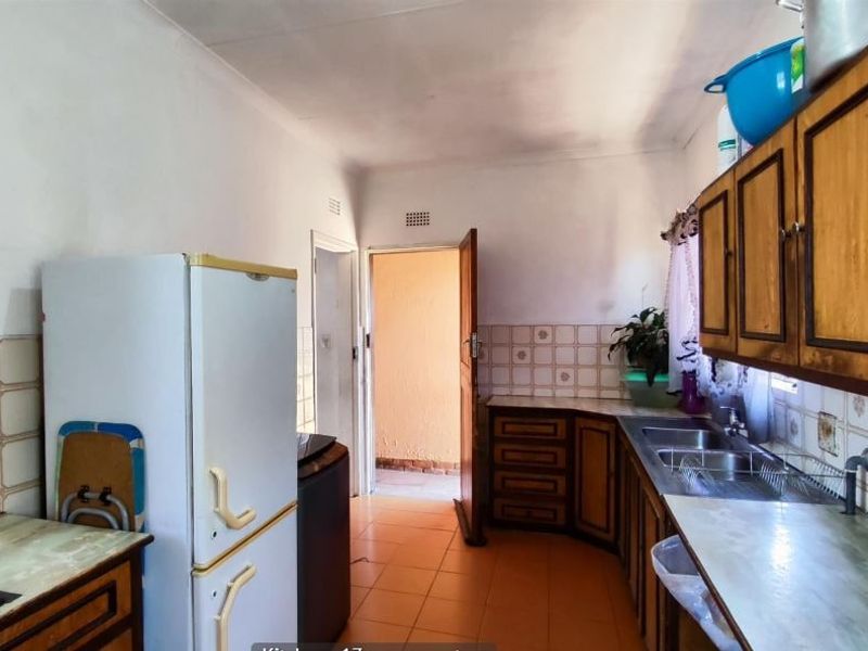 A dated kitchen featuring wooden cabinetry, laminate countertops, and a double sink, with ceramic floor tiles and a tiled backsplash.