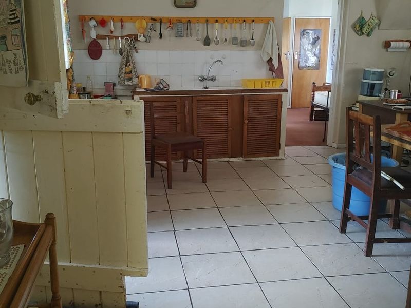 A dated kitchen area featuring tiled flooring, wooden cabinetry, and a tiled splashback, showing signs of wear and wall cracking.