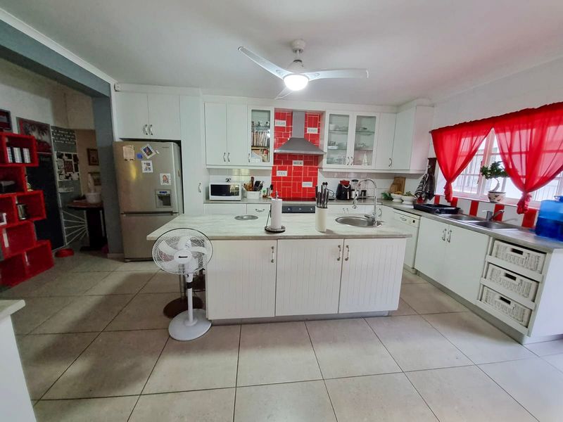 A functional kitchen featuring white cabinetry, a central island with a sink, tiled flooring, and a red tiled backsplash.