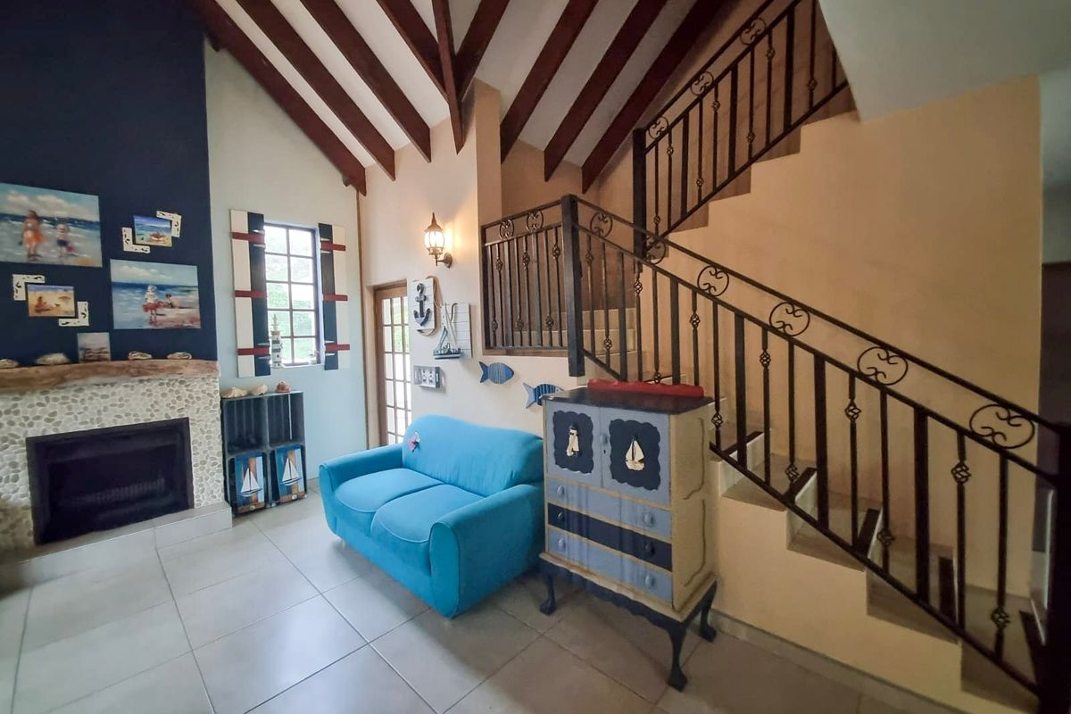 Spacious living room featuring a vaulted ceiling with exposed timber beams, a stone-surround fireplace, and a decorative wrought iron staircase railing.