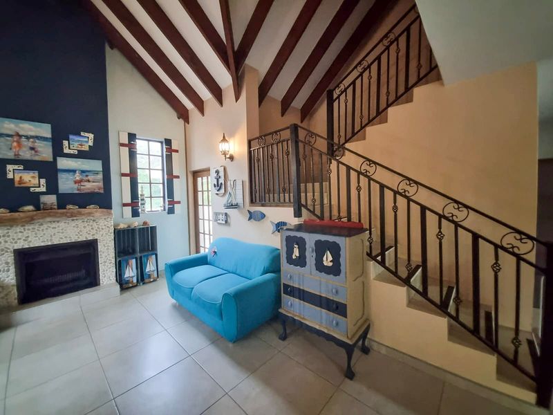 Spacious living room featuring a vaulted ceiling with exposed timber beams, a stone-surround fireplace, and a decorative wrought iron staircase railing.