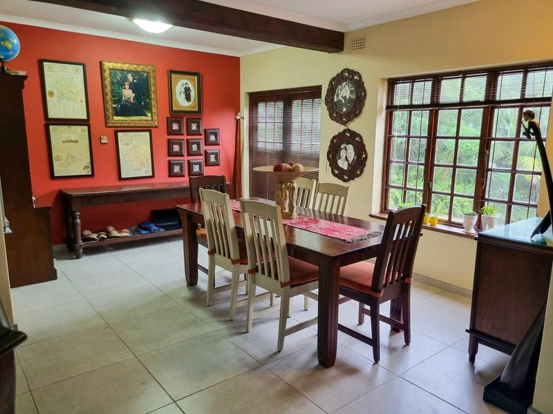 A dining room featuring tiled flooring, exposed timber ceiling beams, and large timber-framed windows with venetian blinds.