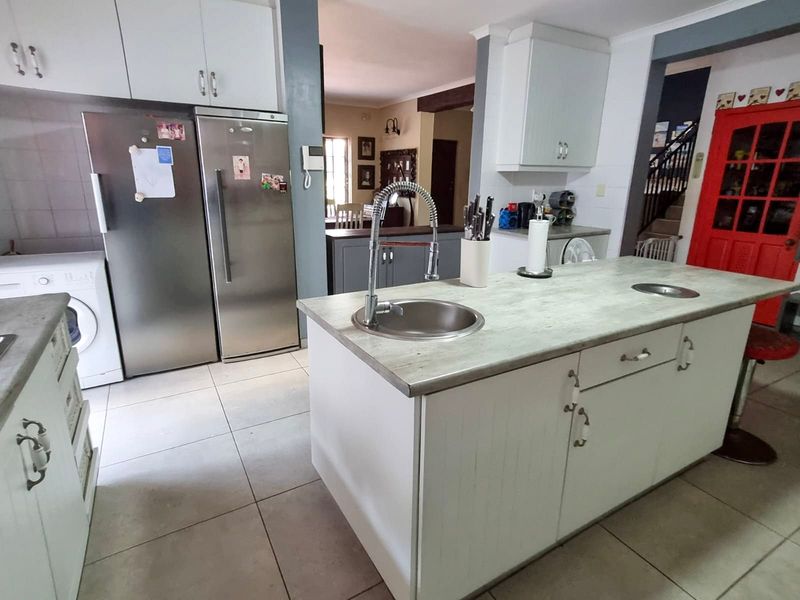 A functional kitchen featuring a central island with a stainless steel sink, ample cabinetry, and tiled flooring, connecting to adjacent living spaces.