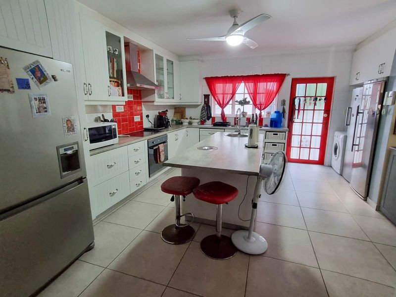 Spacious kitchen featuring a central island, white cabinetry, red tiled splashback, and direct access to the exterior through a glass-panelled door.